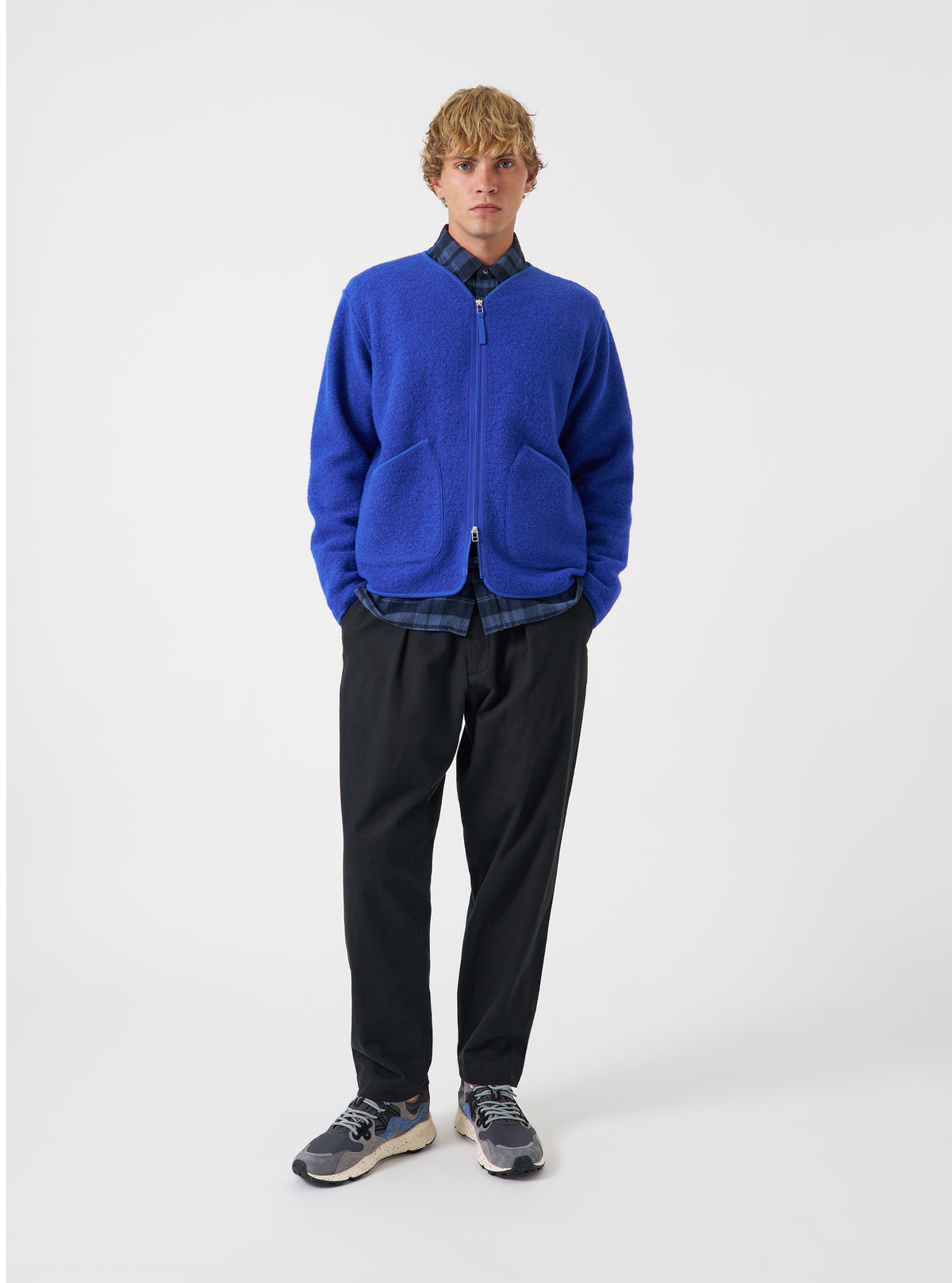 Front view of a model wearing the Blue Wool Fleece Zip Liner Jacket in a bright studio environment. The model stands facing forward, showing how the jacket fits over clothing with its open zipper and blue fleece finish.