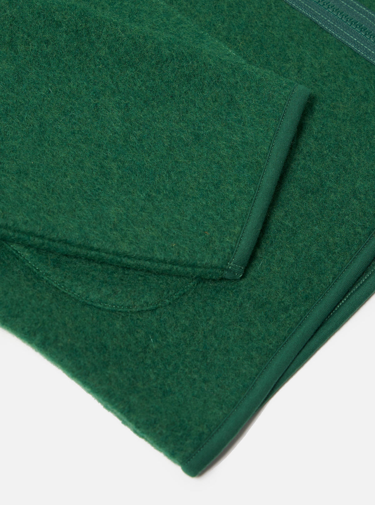 Close-up of the green Wool Fleece Zip Liner Jacket on a white surface. The jacket is made of green wool fleece with a zip. The image shows the texture and details of the jacket.