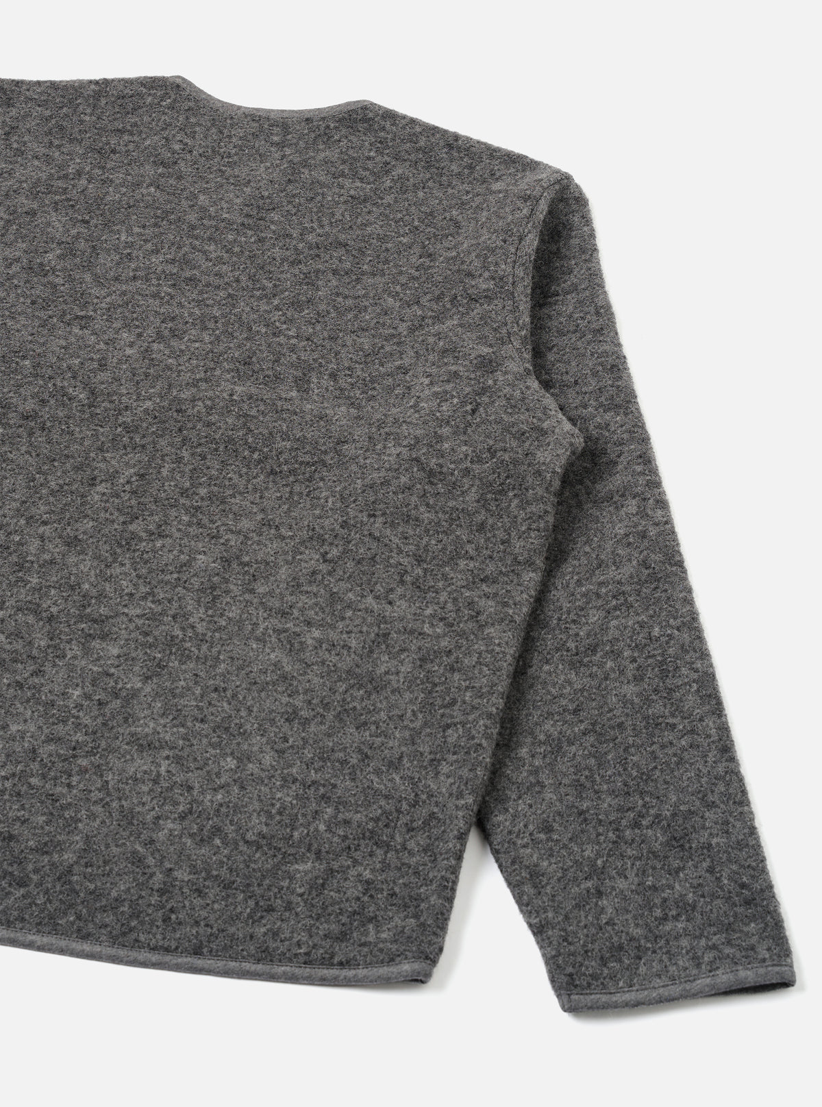 Grey marl wool fleece zip liner jacket, flat lay on a white studio backdrop. Shot shows the back and right sleeve at close range. The boiled wool fleece texture is visible across the body and sleeve. A contrast bound hem runs along the bottom edge. The round neckline is partially visible at the top.