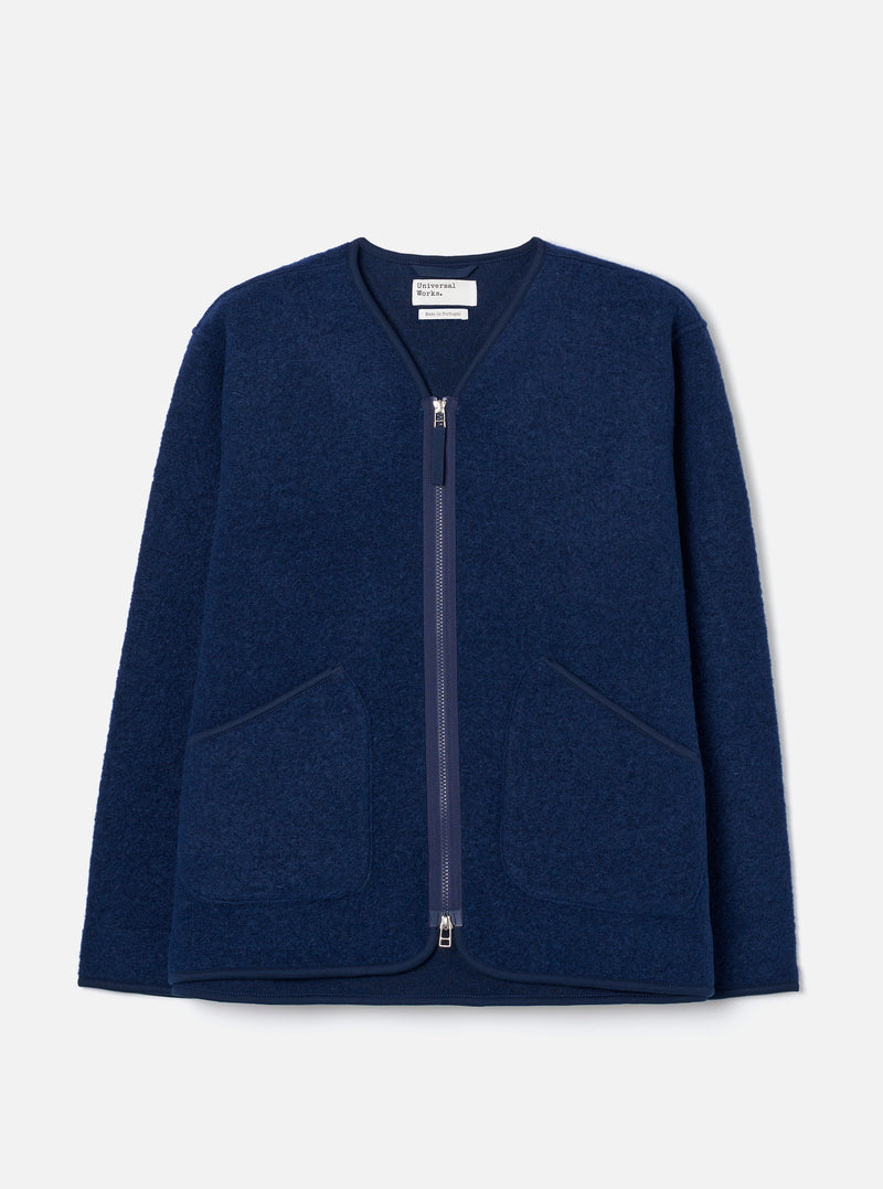 The Indigo Wool Fleece Zip Liner Jacket is laid flat on a light grey backdrop. Features a collarless V-neckline with navy binding, full-length silver zipper, two large patch pockets, and textured boiled wool fleece fabric.