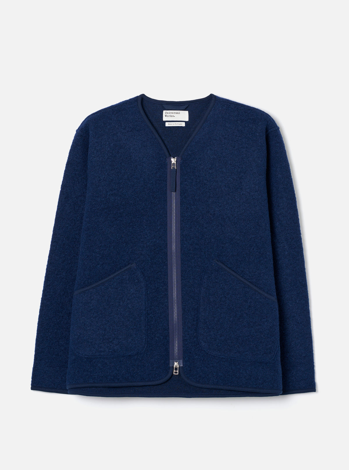 The Indigo Wool Fleece Zip Liner Jacket is laid flat on a light grey backdrop. Features a collarless V-neckline with navy binding, full-length silver zipper, two large patch pockets, and textured boiled wool fleece fabric.