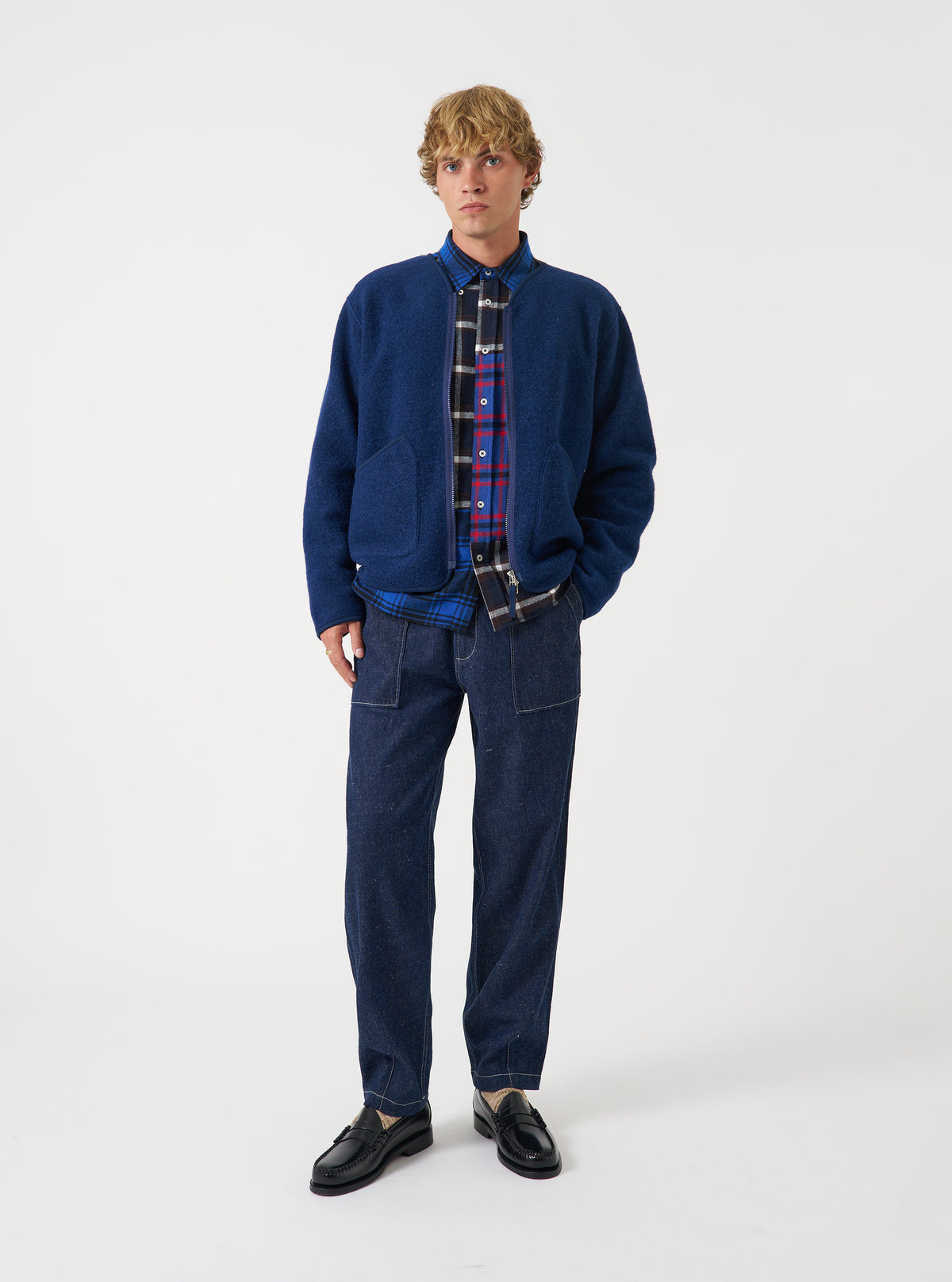 Front view of a model wearing the Indigo Wool Fleece Zip Liner Jacket in a studio environment. The model faces forward, demonstrating the rich indigo blue wool fleece texture, collarless neckline, and zip closure.
