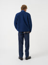 Rear view of a model wearing the Indigo Wool Fleece Zip Liner Jacket against a plain studio backdrop. Showcases the back profile, hemline, and soft deep indigo blue wool fleece material from behind.