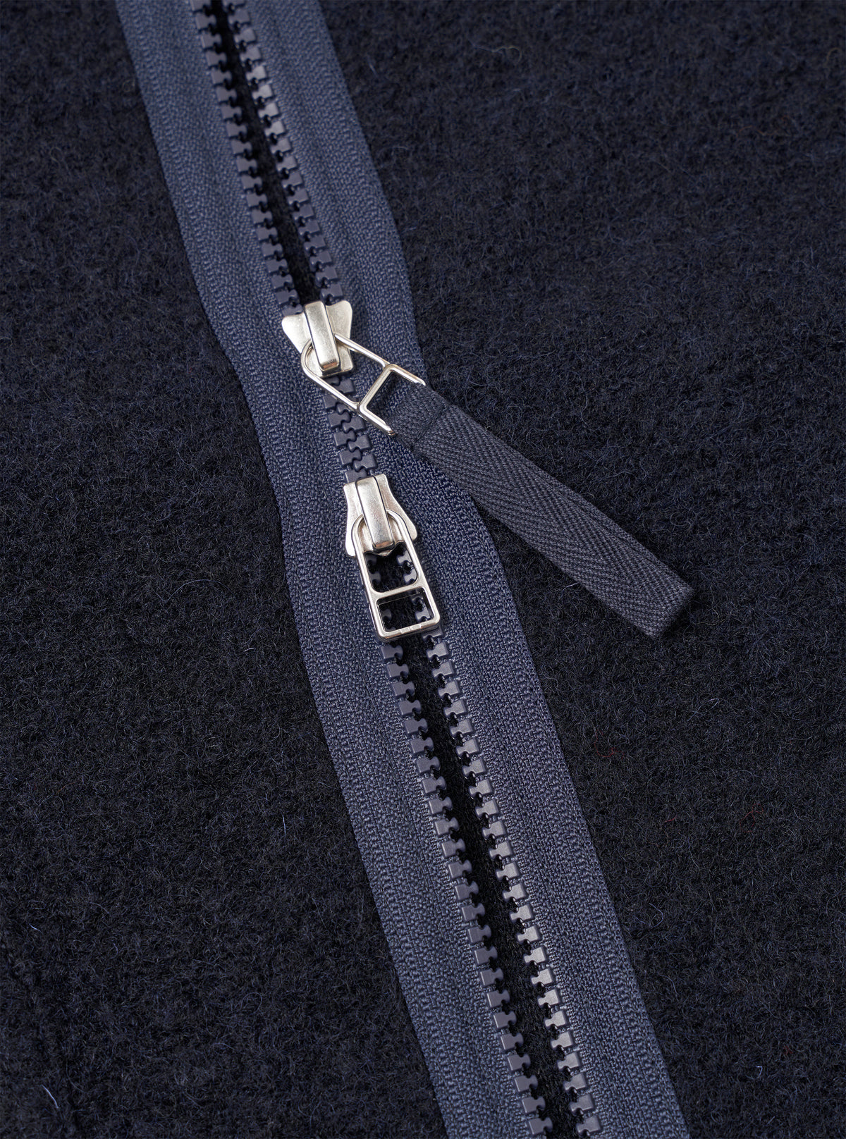 Detailed close-up shot of the Navy Wool Fleece Zip Liner Jacket shown against a clean white background. Highlights the soft textured navy blue wool fleece fabric, sturdy zipper closure, and refined stitching details of the garment.