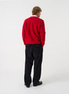 Side angle view of a model wearing the Scarlet Wool Fleece Cardigan in a plain studio setting. Demonstrates the garment fit, relaxed sleeve cut, and rich scarlet red wool fleece material as worn over layered clothing.