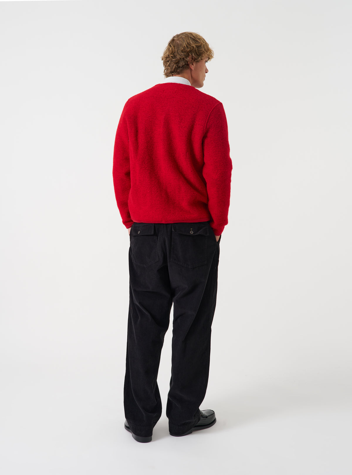 Side angle view of a model wearing the Scarlet Wool Fleece Cardigan in a plain studio setting. Demonstrates the garment fit, relaxed sleeve cut, and rich scarlet red wool fleece material as worn over layered clothing.