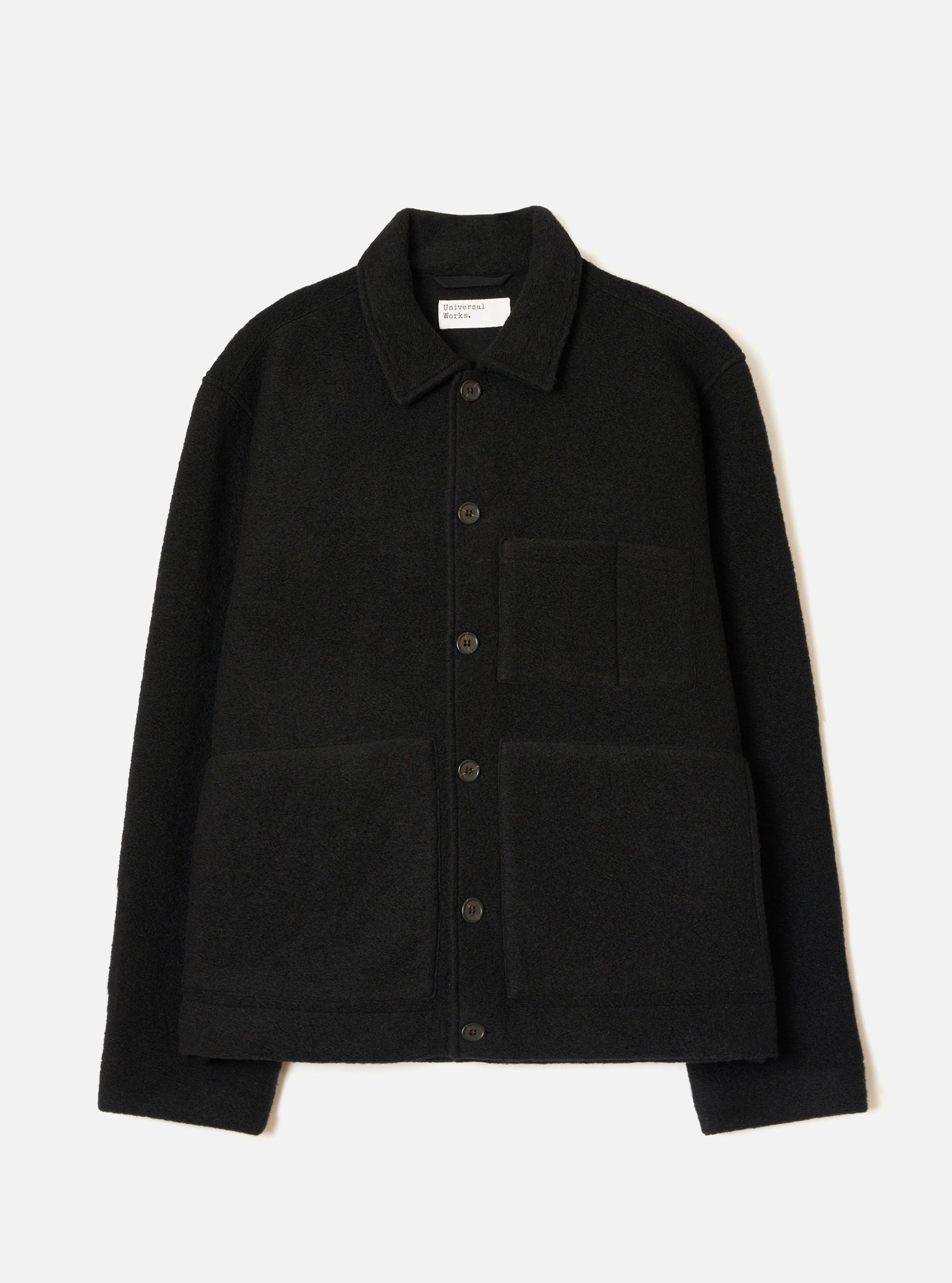 Black wool fleece uniform jacket laid flat on a white studio backdrop. Features a point collar, five dark buttons down the centre front, one chest patch pocket and two large lower patch pockets. The textured boiled wool fleece fabric is visible throughout. A Universal Works woven label sits inside the collar.