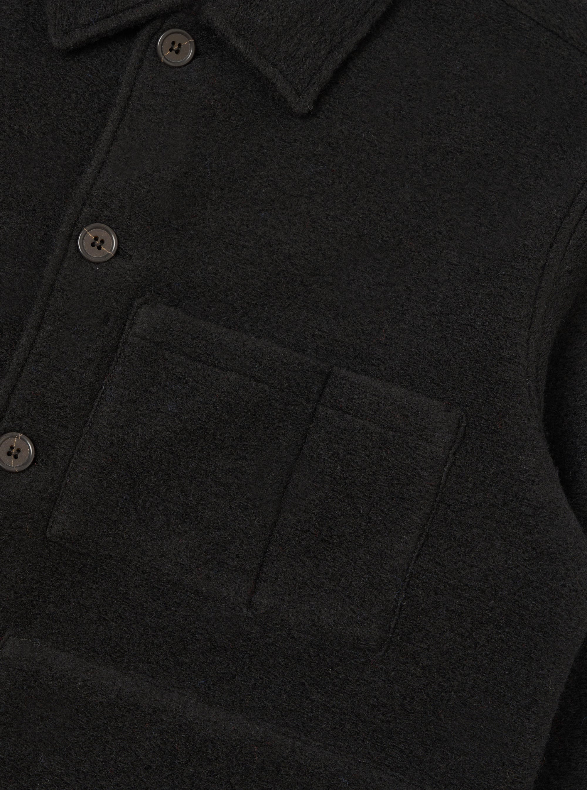 Close-up of a black wool fleece uniform jacket showing the point collar, buttoned placket with dark four-hole buttons, and a large patch chest pocket with an internal divider seam. The brushed fleece texture is clearly visible. No model or mannequin present. Plain dark studio backdrop.