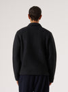 Back view of a male model wearing a black wool fleece uniform jacket against a light grey studio backdrop. The textured fleece fabric is visible across the back panel and full-length sleeves. A spread collar is visible at the neckline. The jacket has a ribbed hem and relaxed fit. Worn over navy trousers. Shot cropped from mid-thigh up.