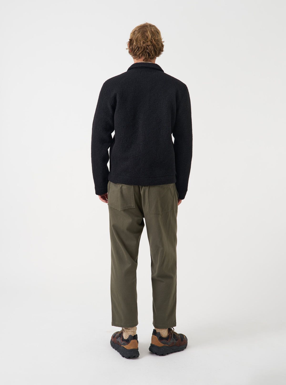 Angled view of a model wearing the Black Wool Fleece Uniform Jacket in a clean studio setting. Highlights the comfortable fit, soft black wool fleece material, shoulder construction, and overall profile of the jacket.
