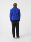 Three-quarter view of a model wearing the Blue Wool Fleece Uniform Jacket in a plain studio space. Highlights the textured blue fleece fabric, side profile fit, sleeve cuff finishing, and overall casual jacket styling.