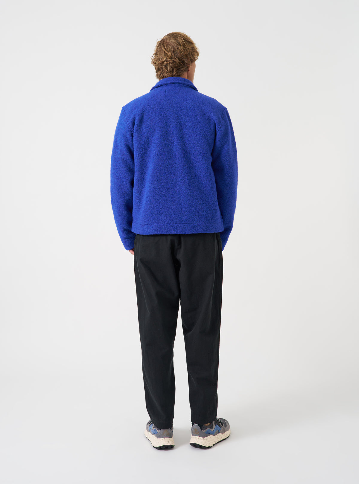 Three-quarter view of a model wearing the Blue Wool Fleece Uniform Jacket in a plain studio space. Highlights the textured blue fleece fabric, side profile fit, sleeve cuff finishing, and overall casual jacket styling.