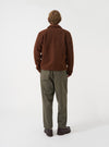 Back view of a model wearing the Cacao Wool Fleece Uniform Jacket against a plain studio backdrop. The model stands turned away, showing the jacket's smooth back panel, relaxed fit, and rich cacao brown wool fleece texture.