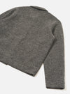 Close-up flat lay of a grey marl wool fleece uniform jacket on a white studio surface, shot from above at an angle. The back panel and one sleeve are visible, showing the soft, lightly textured boiled wool fleece fabric. A small collar is visible at the top. The sleeve ends in a plain, clean-finished cuff.