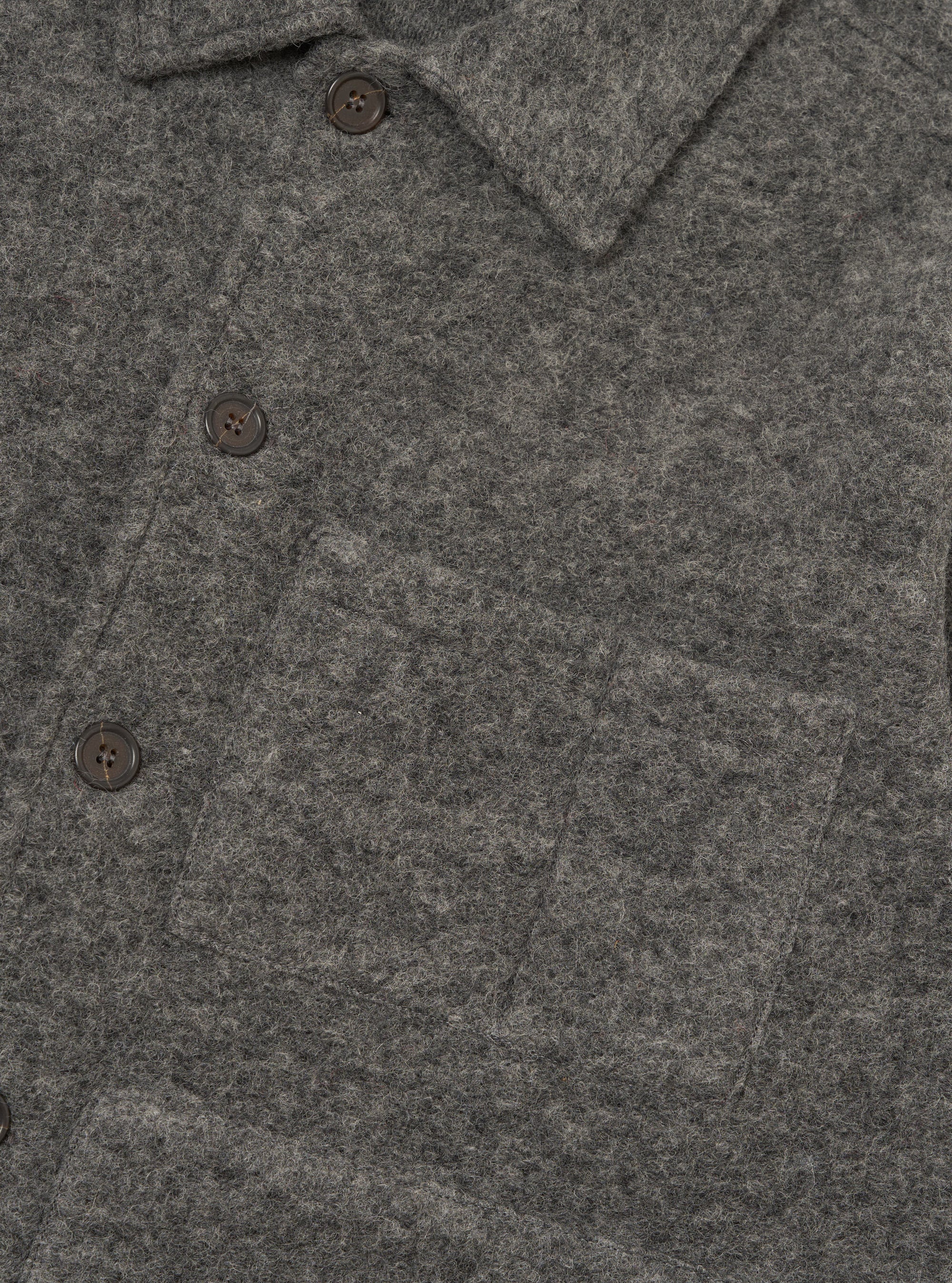 Close-up of a grey marl wool fleece uniform jacket on a plain white backdrop. The shot shows the spread collar, three dark horn-effect buttons on the placket, and a large patch pocket visible on the chest. The brushed, fleecy wool texture is prominent across the fabric.