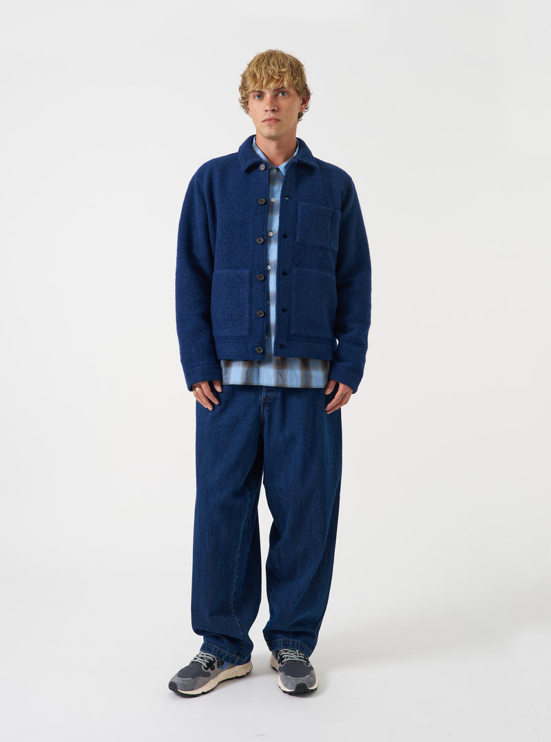 Front view of a model wearing the Indigo Wool Fleece Uniform Jacket in a plain studio setting. The model faces forward, displaying the dark indigo blue fleece texture, classic collar, button placket, and front patch pockets.
