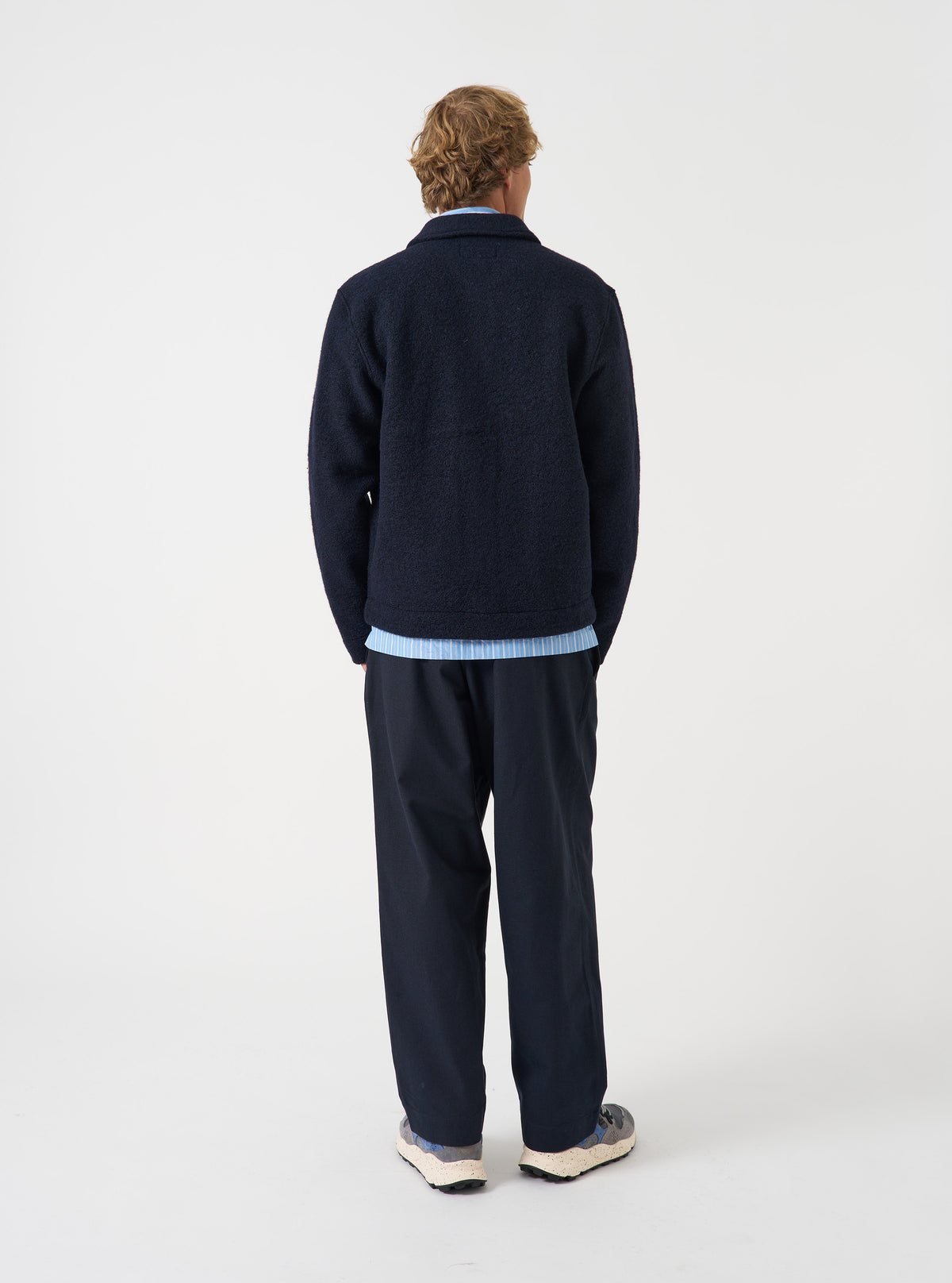 Rear view of a model wearing the Navy Wool Fleece Uniform Jacket in a studio setting with a light backdrop. The image displays the plain back construction, shoulder seams, and dark navy wool fleece fabric texture.