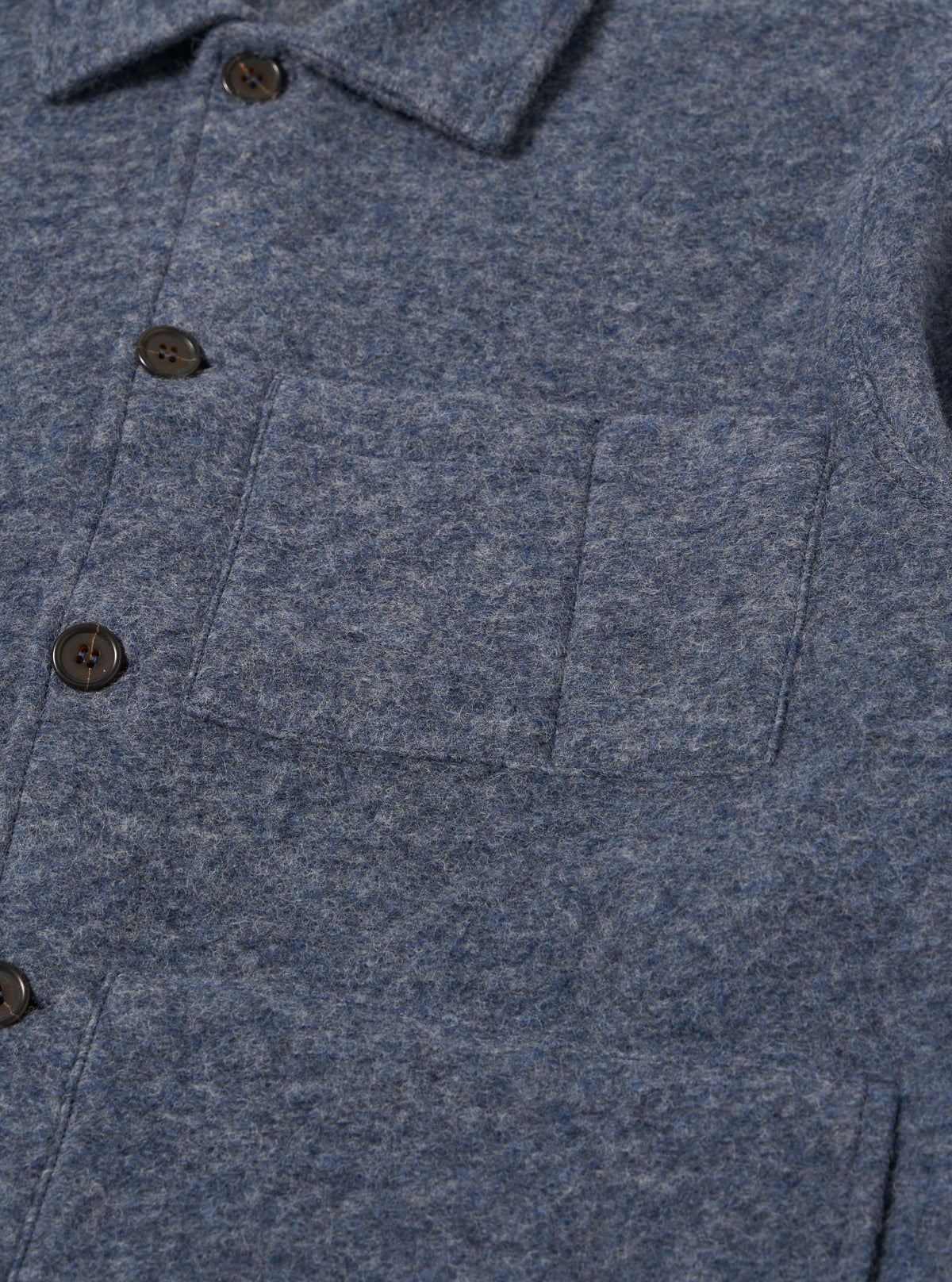 Close-up of the slate blue wool fleece uniform jacket showing the texture, buttons, and pocket. The jacket is on a flat surface.