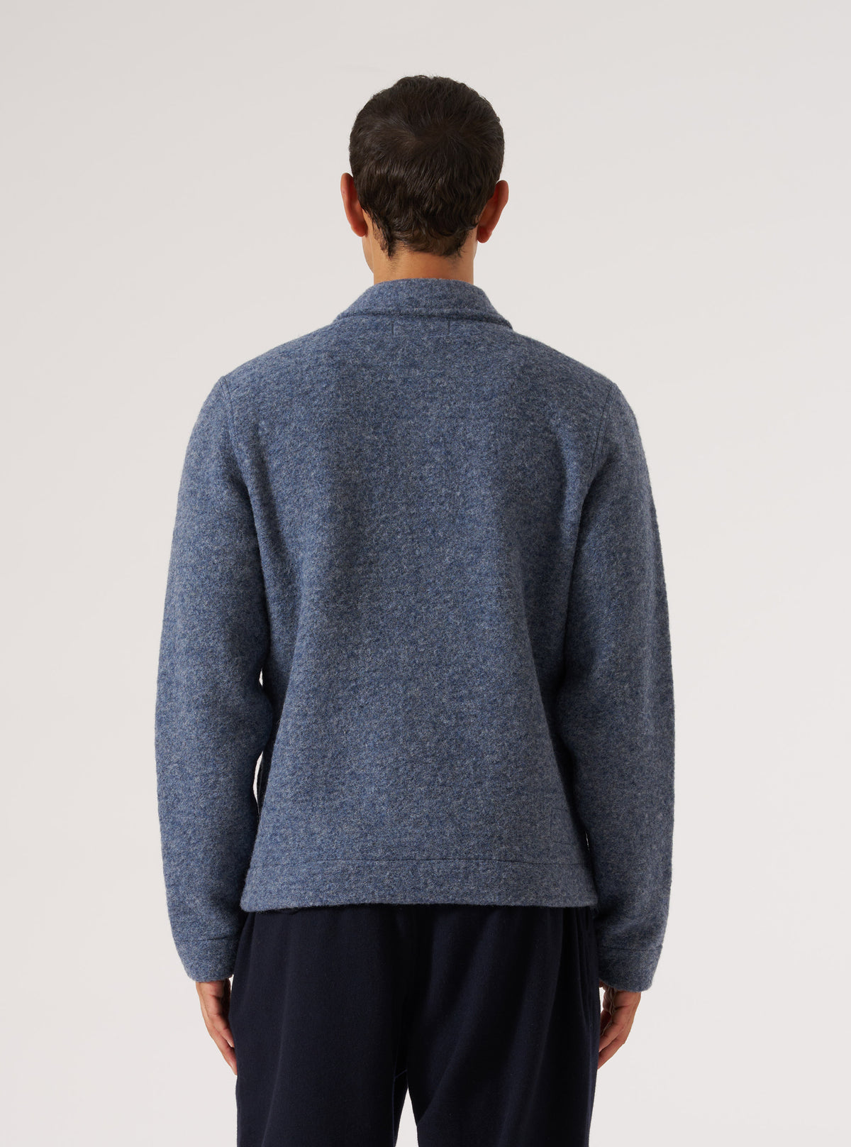 Back view of a model wearing a Slate Blue Wool Fleece Uniform Jacket. The jacket is on a white background and paired with dark pants.
