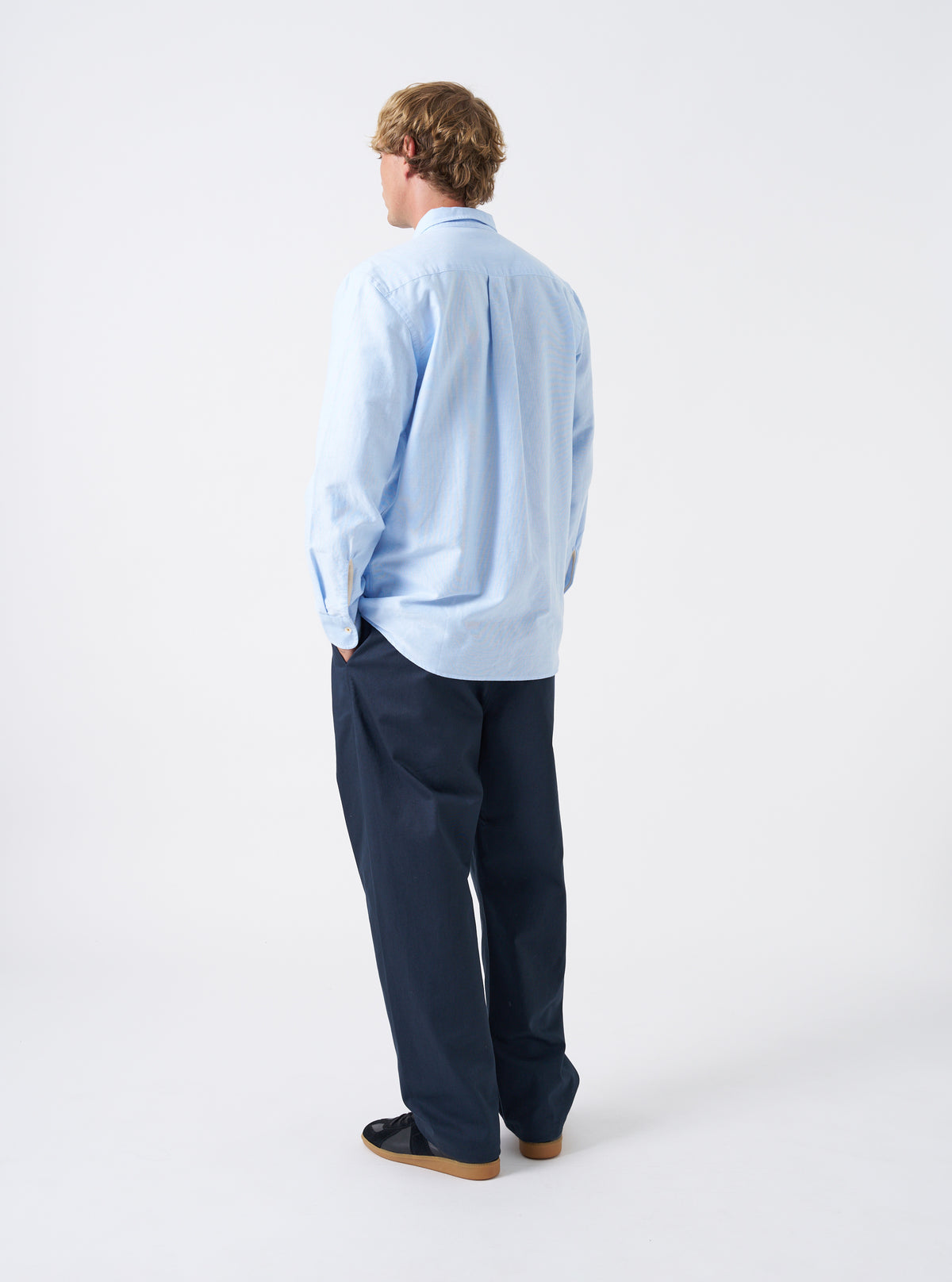 Angled view of a model wearing the Sky Blue Oxford Daybrook Shirt against a plain studio background. Highlights the side profile fit, sleeve drape, cuff finish, and classic casual look of the organic oxford garment.