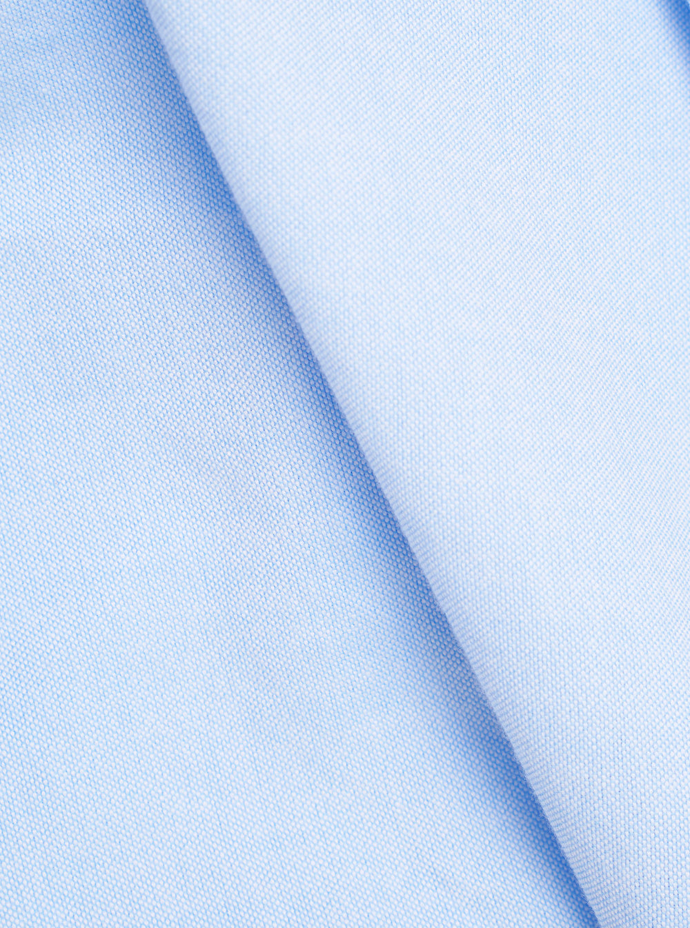 Extreme close-up fabric swatch image showcasing the texture of the Sky Blue Oxford Daybrook Shirt. The detailed macro shot highlights the pale blue color threads and distinct basketweave structure of the organic cotton oxford.