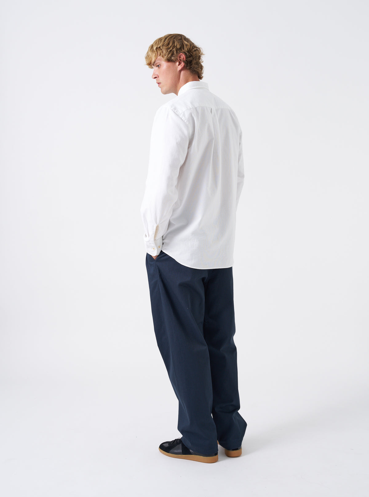 Side angled view of a model wearing the White Oxford Daybrook Shirt against a light backdrop. The image emphasizes the tailored fit along the body, sleeve cuffing, and clean style of the organic cotton shirt.