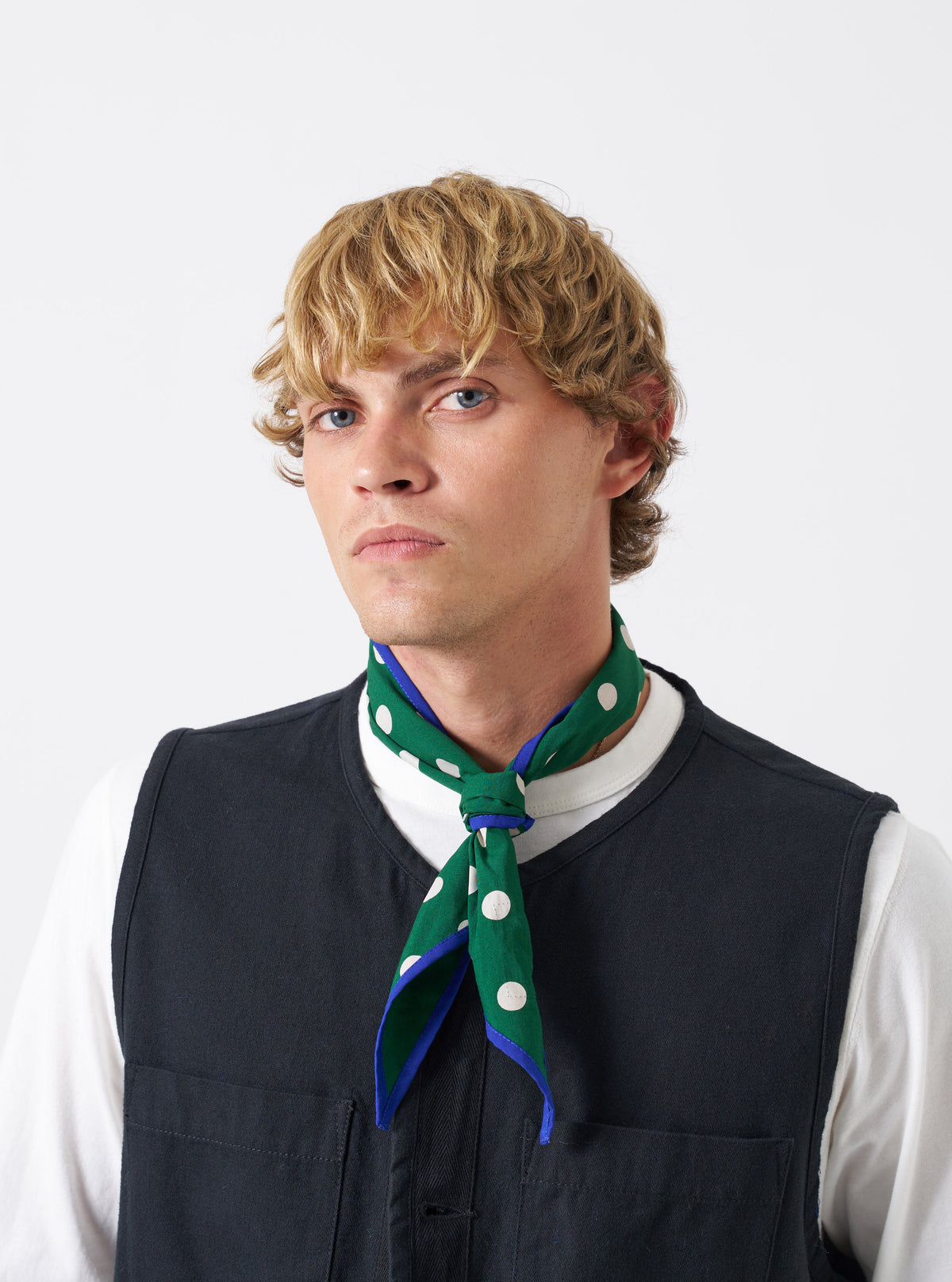 A model wearing the Forest Green Bold Dot Print Rayon Scout Scarf in a plain studio environment. The scarf is tied around the neck, highlighting its deep green tone and bold polka dot print against the backdrop.
