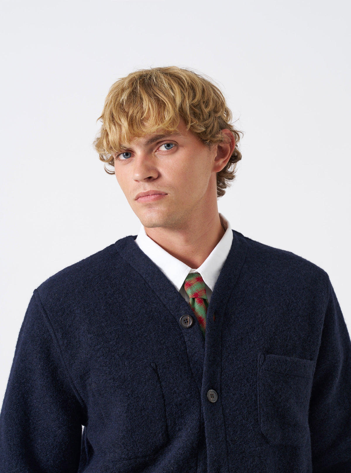 A model wearing the Red/Green/Mustard Sound Wave Rayon Tie in a studio setting with a plain background. The tie is worn neatly around the collar, showcasing its intricate geometric pattern and vibrant color palette.