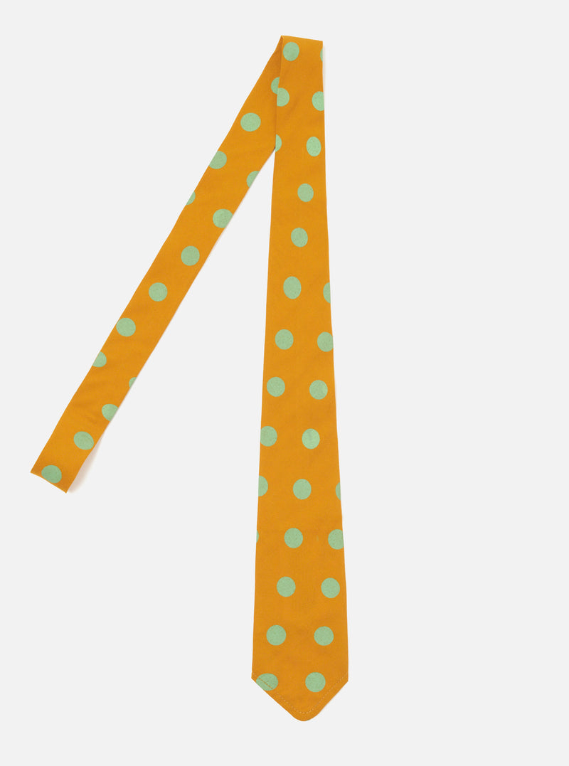 The Mustard Bold Dot Print Rayon Tie on a white surface. The tie is mustard yellow with bold green dots. The tie is made of rayon.