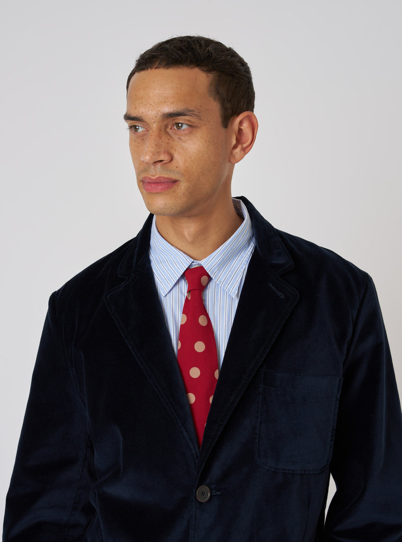 A model wears a Red Bold Dot Print Rayon Tie with a blue striped shirt and navy blazer against a white background.