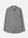 Grey chambray Daybrook shirt by Universal Works, flat lay on a light grey seamless backdrop. Button-down collar with buttoned collar points, full button placket with white buttons, single chest patch pocket, and long sleeves with buttoned cuffs. Fine woven texture visible throughout. Curved hem. Universal Works woven label at neck.