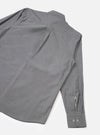 Flat lay of the Black Prince chambray Daybrook shirt on a white studio backdrop, showing the back and one sleeve. The fine-weave grey chambray fabric has a subtle texture. A back yoke seam runs across the shoulders. The cuff is buttoned with two small grey buttons and features a placket opening.