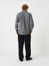 Back view of a male model wearing the Black Prince Chambray Daybrook Shirt against a light grey studio backdrop. The shot shows the back panel, rear yoke seam, central pleat, and long sleeves of the textured black cotton shirt.