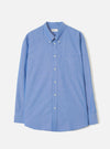 Blue chambray shirt laid flat on a light grey backdrop. Features a button-down collar, front button placket with white buttons, a single chest patch pocket, long sleeves with buttoned cuffs, and a curved hem. The fine woven texture of the chambray fabric is visible throughout.