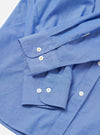 Close-up flat lay of the blue chambray Daybrook shirt on a white surface, focusing on two long sleeves and their cuffs. Each barrel cuff features two cream buttons with cross stitching. Top-stitching details the cuff edges and placket. The fine chambray weave is visible throughout.