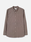 Brown chambray long-sleeve shirt laid flat on a light grey studio backdrop. Button-down collar with a Universal Works woven label at the back neck. Seven pale buttons down the placket, one chest patch pocket on the left, and single-button barrel cuffs. Fine woven texture with a subtle two-tone weave. Curved hem.
