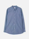 Indigo chambray long-sleeve shirt laid flat on a light grey background. Features a button-down collar, centre-front button placket with white buttons, a left-chest patch pocket, and barrel cuffs. The curved shirttail hem is visible at the base. Fine chambray weave texture throughout.