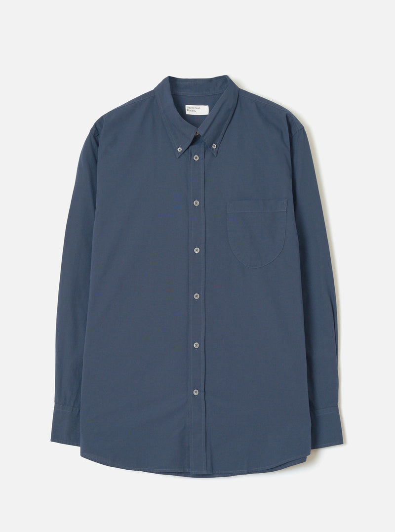 Front view of the Navy Prince Chambray Daybrook Shirt laid flat on a light grey studio backdrop. Features a spread collar, full button closure down the front, single chest patch pocket, and long sleeves with buttoned cuffs. No model present.