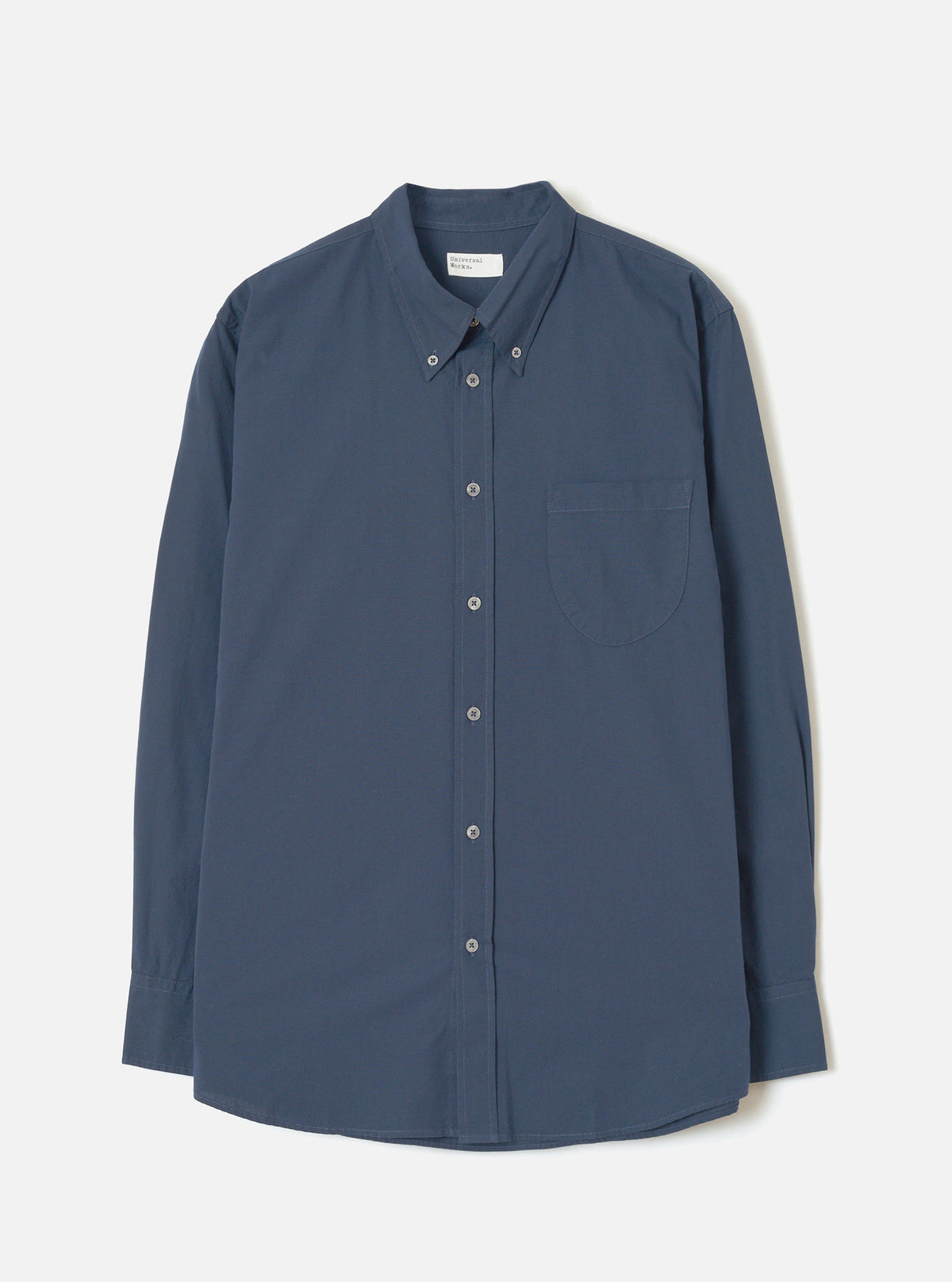 Front view of the Navy Prince Chambray Daybrook Shirt laid flat on a light grey studio backdrop. Features a spread collar, full button closure down the front, single chest patch pocket, and long sleeves with buttoned cuffs. No model present.