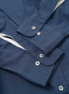 Close-up flat lay of the navy chambray Daybrook shirt showing two buttoned barrel cuffs with silver four-hole buttons. A cream cotton twill tape trim is visible along the placket edge. The plain-weave fabric has a fine texture. Top-stitching details the cuff edges. Shot on a white studio surface.