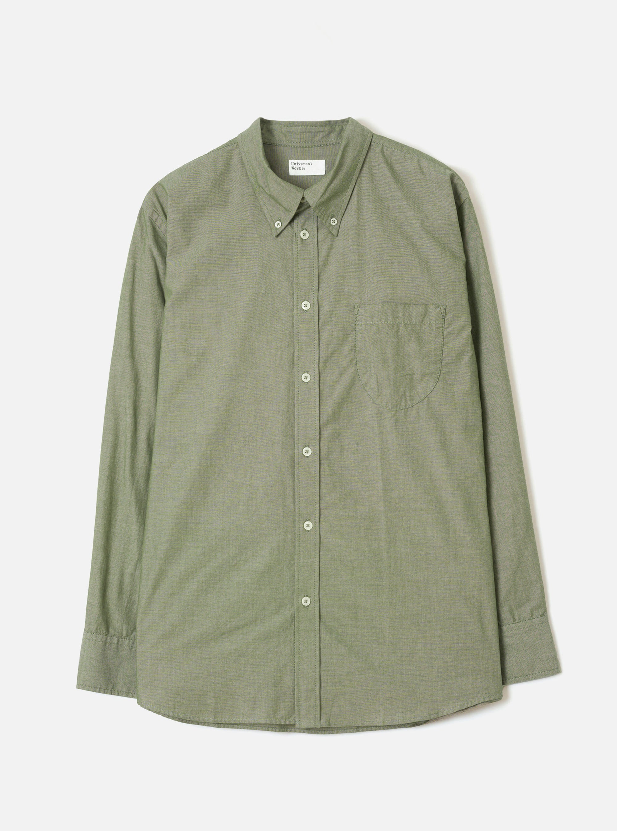 Olive chambray long-sleeve shirt laid flat on a light grey background. Button-down collar with collar buttons visible, full button placket with five cream buttons, single chest patch pocket on the left, buttoned cuffs, and a curved hem. Fine woven texture throughout. Universal Works woven label at the neck.