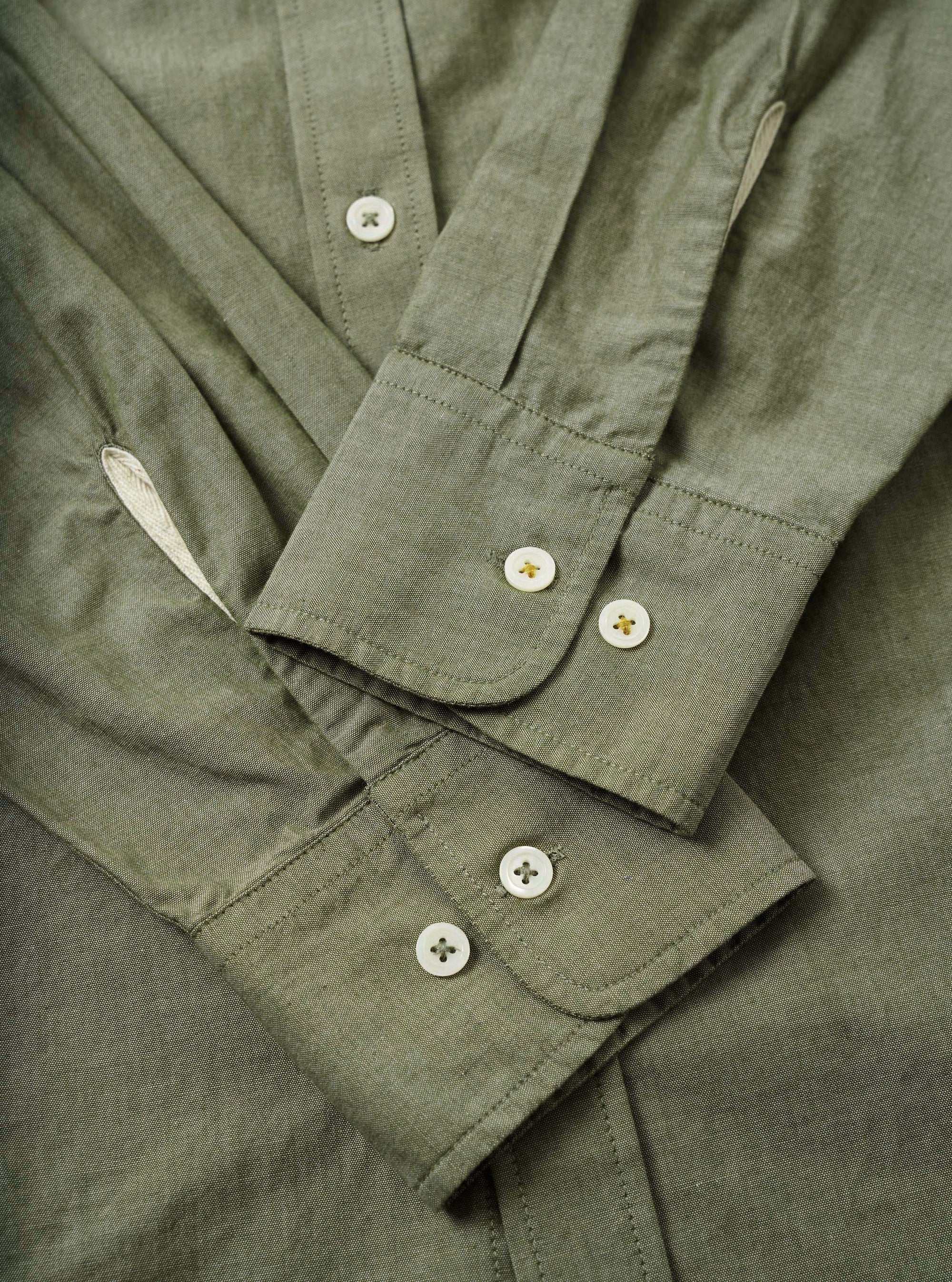 Close-up flat-lay detail of the olive chambray Daybrook shirt, showing two barrel cuffs each fastened with two white four-hole buttons with gold stitching. The placket is visible at the top with a single button. Fine topstitching runs along the cuff edges. The woven chambray fabric has a subtle two-tone texture.