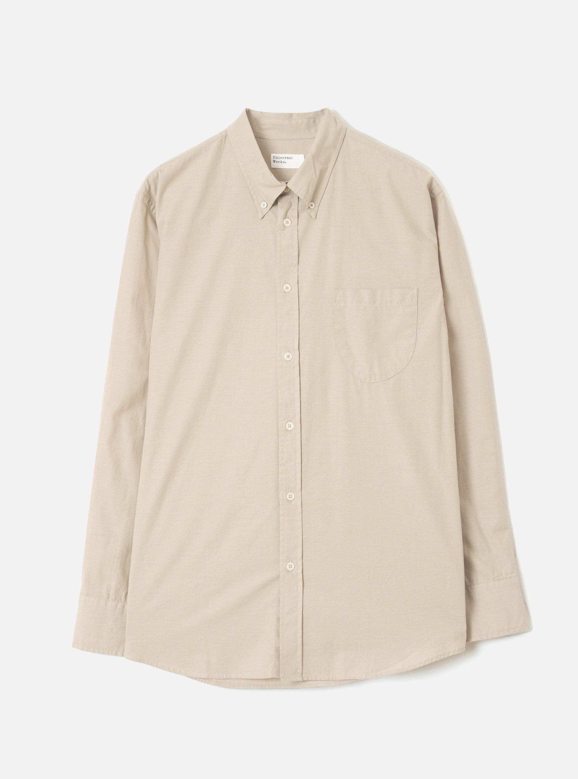 Sand chambray Daybrook shirt laid flat on a white studio backdrop. Button-down collar with tonal buttons down the placket, a single patch pocket on the left chest, long sleeves with plain cuffs, and a curved hem. Plain weave fabric in a warm sand tone.