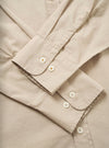 Close-up flat lay of a sand-coloured chambray shirt, focusing on both cuffs. Each single-button cuff features two white mother-of-pearl buttons on a rounded placket with visible topstitching. A placket with a third button is visible at the top of the frame. The plain-weave cotton fabric has a fine, smooth texture.