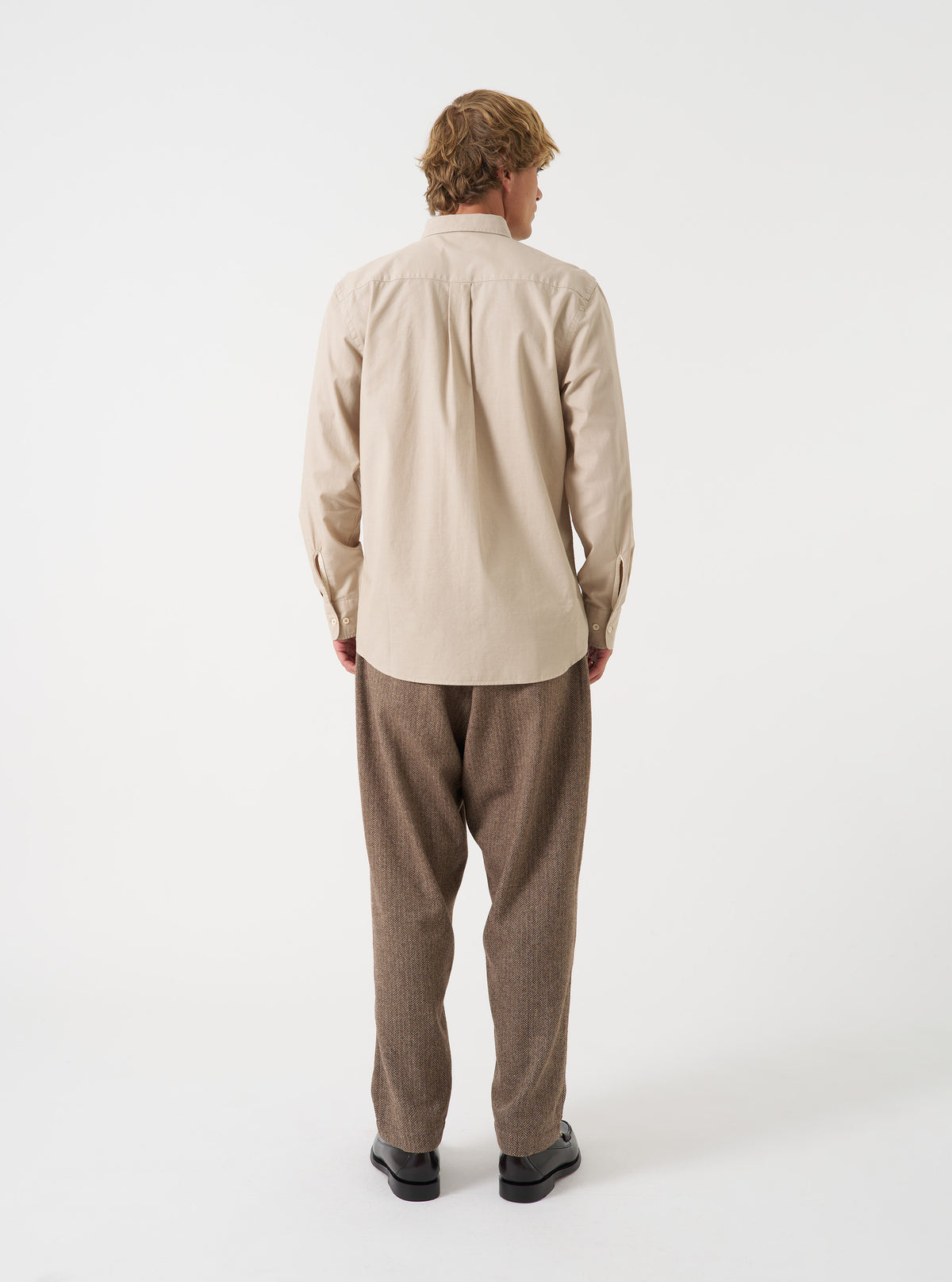 Back view of a male model wearing the Sand Prince Chambray Daybrook Shirt against a plain studio background. The light tan cotton fabric features a visible back yoke, neat shoulder seams, and a relaxed straight fit.