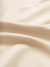 Close-up of the sand-coloured chambray fabric used in the Daybrook Shirt. The fine woven texture is clearly visible, with soft natural folds creating gentle shadow and depth across the cream-toned cloth.