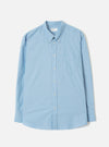 Sky blue chambray long-sleeve shirt laid flat on a light grey seamless backdrop. Button-down collar with a woven Universal Works label at the neck. Centre front button placket with white buttons. Single patch chest pocket on the left. Rounded shirt tail hem and plain cuffs.