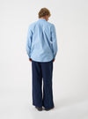 Side view of a model wearing the Sky Blue Prince Chambray Daybrook Shirt against a plain studio background. The model is shown from the waist up, displaying the light blue cotton chambray texture, classic collar, and button-down front.