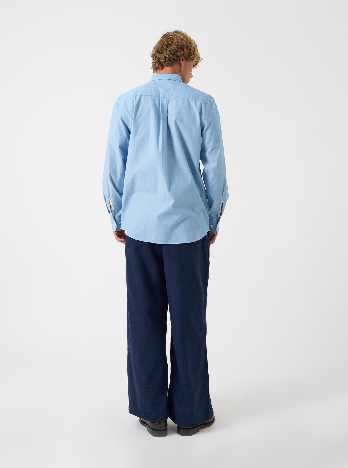 Side view of a model wearing the Sky Blue Prince Chambray Daybrook Shirt against a plain studio background. The model is shown from the waist up, displaying the light blue cotton chambray texture, classic collar, and button-down front.