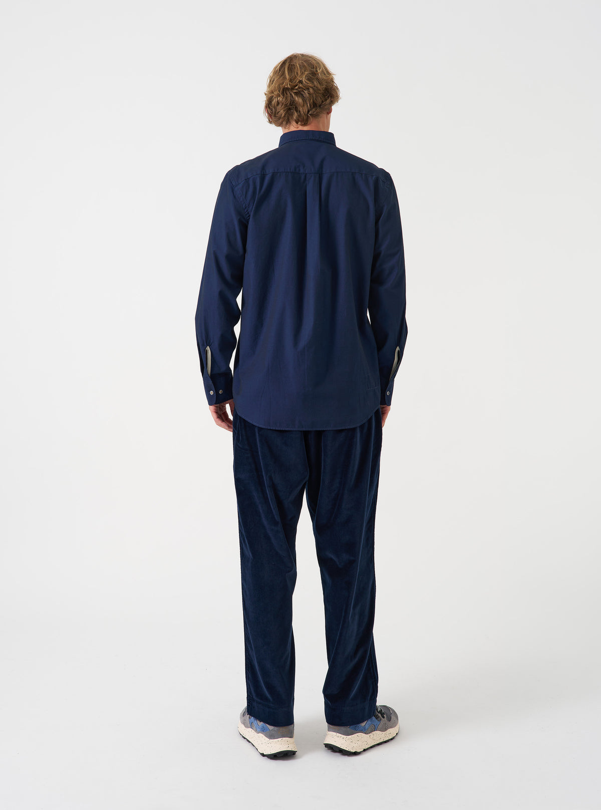 Angled view of a model wearing the Navy Prince Chambray Daybrook Shirt against a simple studio backdrop. Highlights the overall fit, sleeve cut, buttoned cuffs, and fine navy prince chambray cotton fabric.